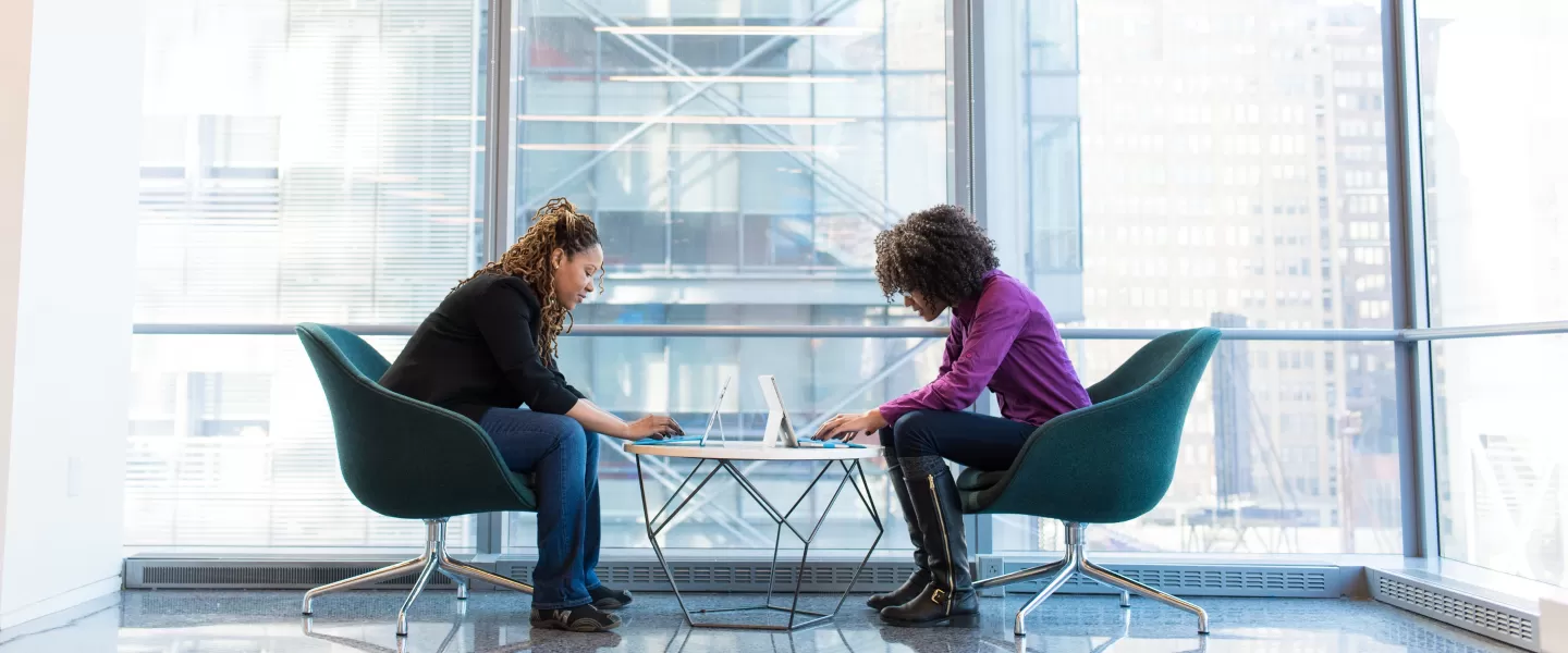 Dwie kobiety siedzące naprzeciwko siebie, używające laptopów