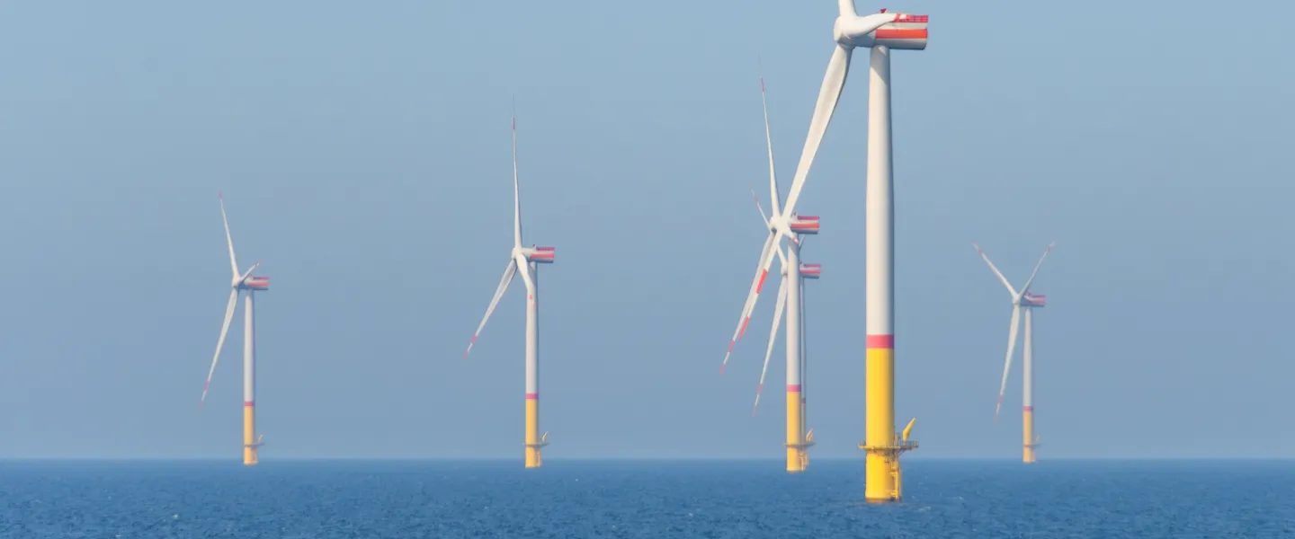 Morskie turbiny wiatrowe ustawione na otwartym morzu, widoczne na tle jasnego, bezchmurnego nieba